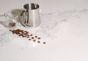 a silver pitcher and coffee beans on a marble surface
